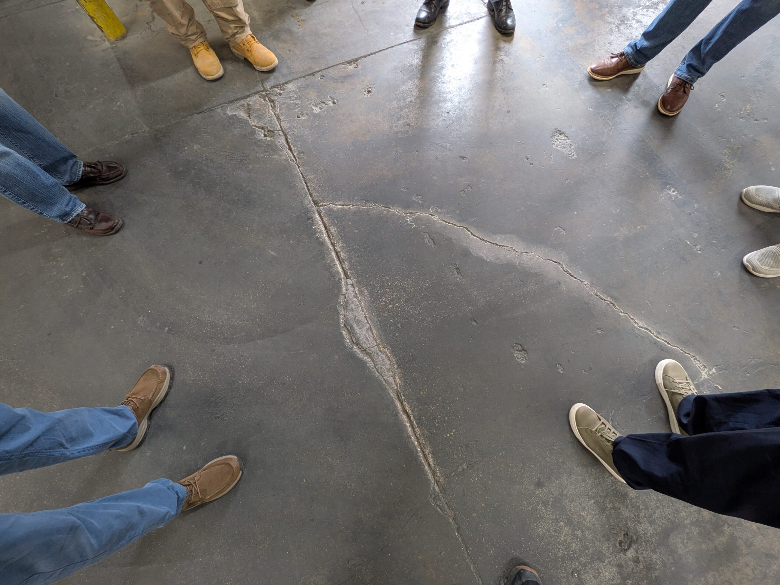 PXL_20250605_162821852 Overhead photo of concrete warehouse with people looking at floor crack before being repaired with FasTrac Crackweld Pro.